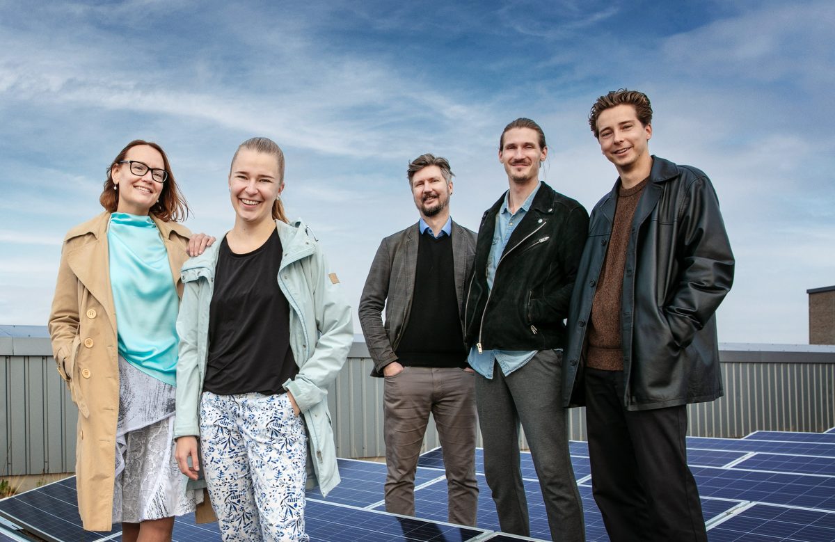 Taloyhtiöiden energianeuvonnan asiantuntijat talon katolla, taustalla aurinkopaneelit