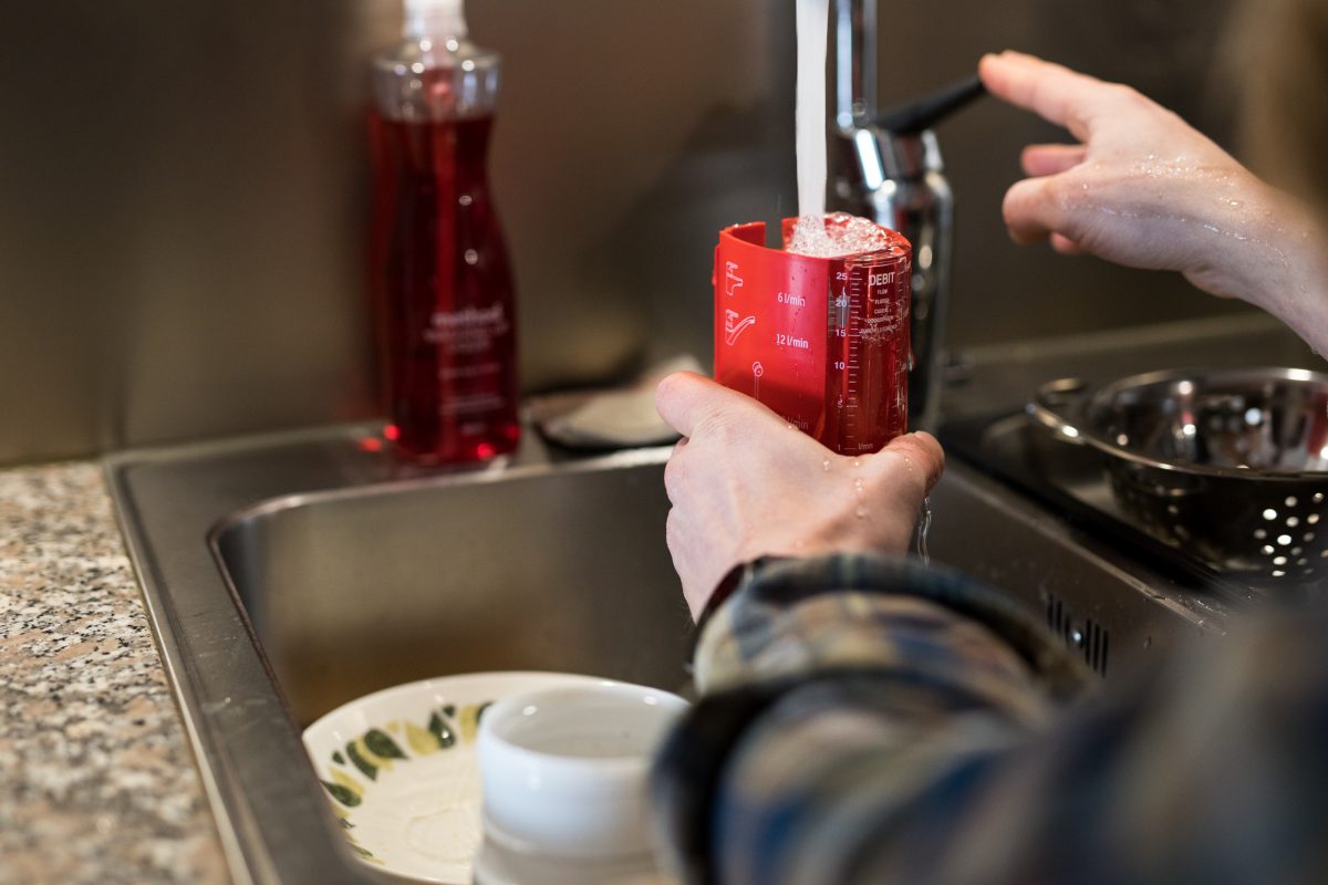 Henkilö valuttaa vettä keittiönhanasta vesivirtaamakuppiin.